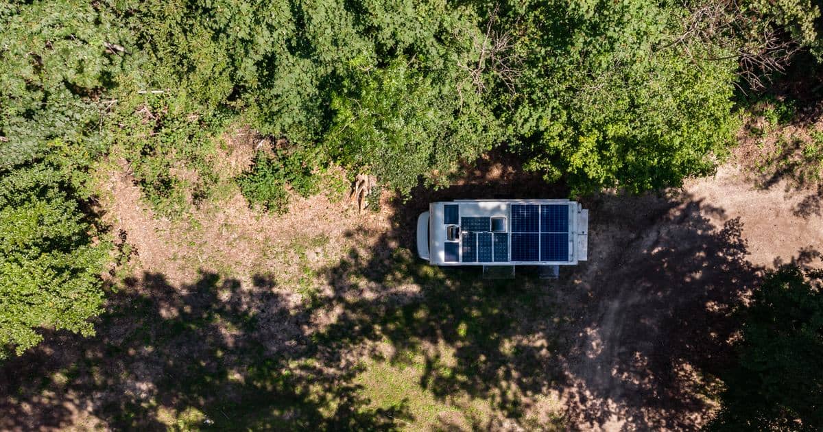 Luftfoto av en bobil med solcellepaneler på taket parkert i en skogsåpning