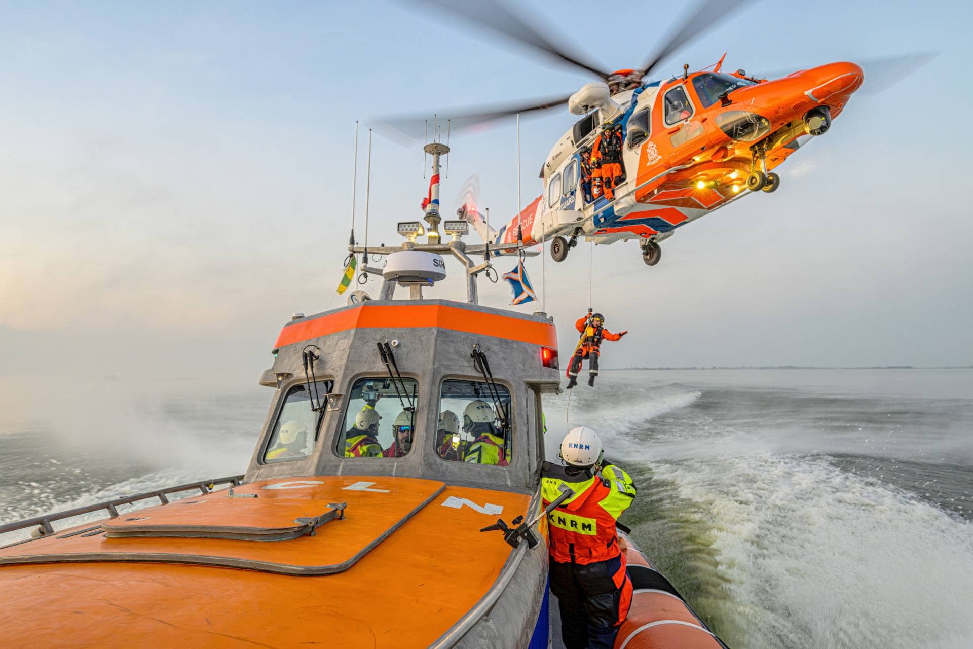 KNRM redningsbåt på sjøen med et redningshelikopter som heiser opp et besetningsmedlem