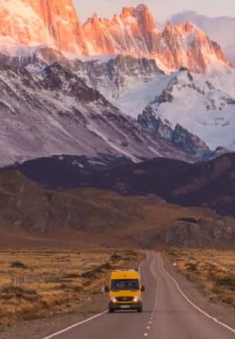 Gul campingbil på en åpen vei nedenfor det snødekte Fitz Roy-massivet i Patagonia